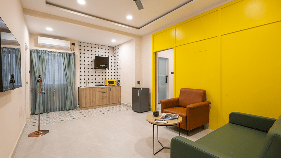 Studio Suite living room with a green sofa, tan armchair, coffee table, yellow sliding door and kitchenette at Monday Hotels & Suites Madhapur, Hyderabad.