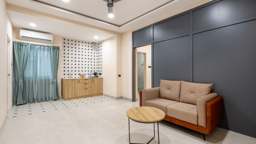 A living area featuring a sofa, coffee table, ceiling fan, and kitchenette counter against a dark accent wall at Monday Hotels & Suites Madhapur Hyderabad.