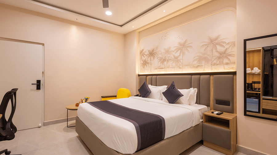 Premium room with a king bed, palm mural, bedside table and a wall mirror reflecting the wardrobe unit at Monday Hotels & Suites Madhapur, Hyderabad.