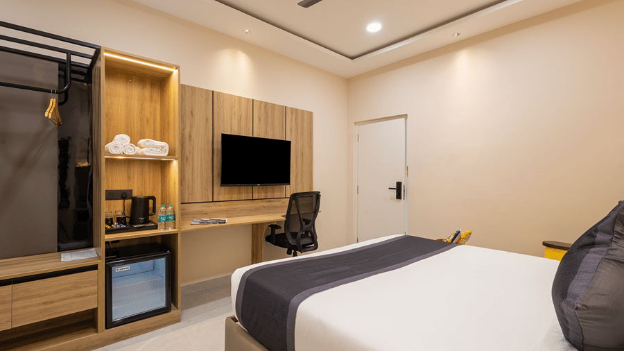 Open wardrobe, towel shelves, kettle, minibar, wall-mounted TV and work desk beside the bed in a Premium room at Monday Hotels & Suites Madhapur, Hyderabad.