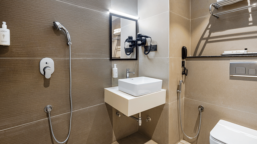 The bathroom at rooms of Monday Premium, Madhapur, featuring a handheld shower, a sink, a mirror, and a toilet seat.