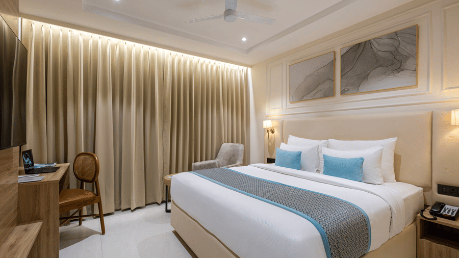 A room at Monday Premium, Madhapur, featuring a large bed, bedspreads, pillows, a table, a chair, and windows covered with curtains.