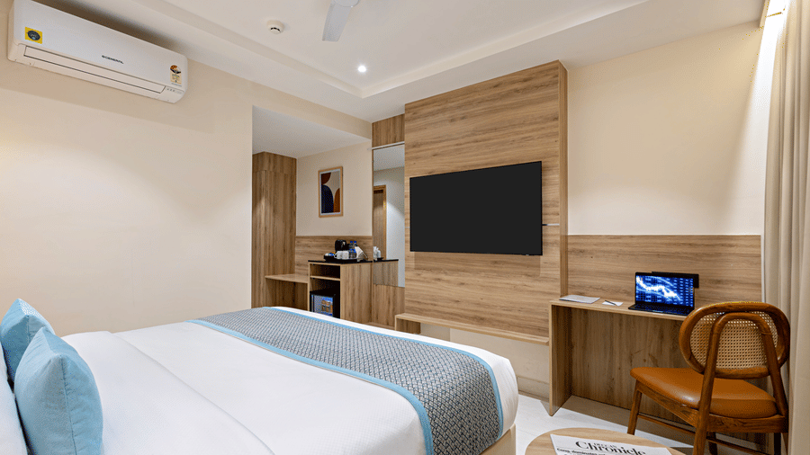 A room at Monday Premium, Madhapur, featuring a large bed, bedspreads, pillows, a table, a chair, a television, and a wallmounted air-conditioner.