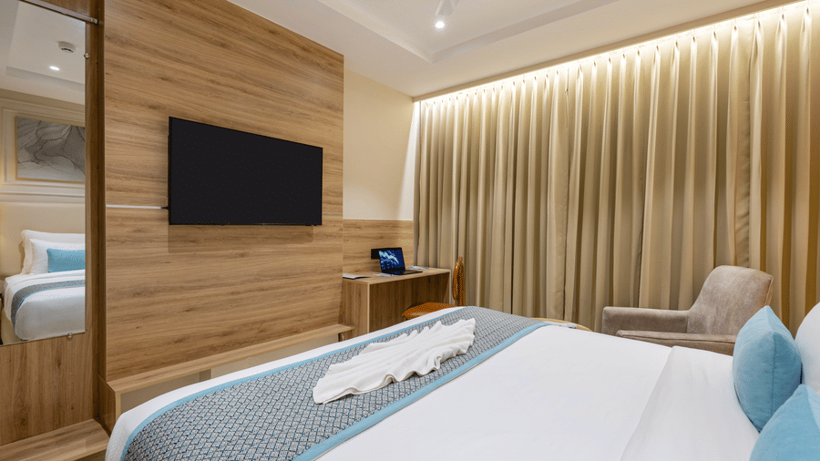 A room at Monday Premium, Madhapur, featuring a large bed, bedspreads, pillows, a table, a cushion, a television, and a mirror.