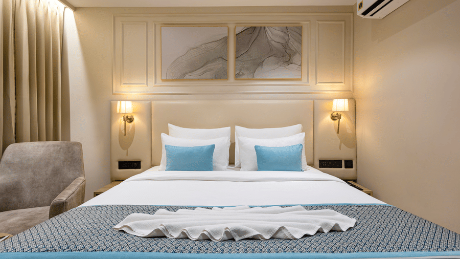 A room at Monday Premium, Madhapur, featuring a large bed, bedspreads, pillows, lamps, a cushion, windows, and a wall mounted air-conditioner.