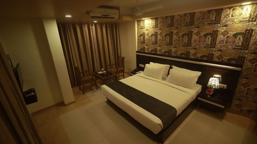 A Deluxe Room of Mountview Resort furnished with a king size bed, a wall-mounted TV, bedside tables, and a seating area in front of closed curtains.