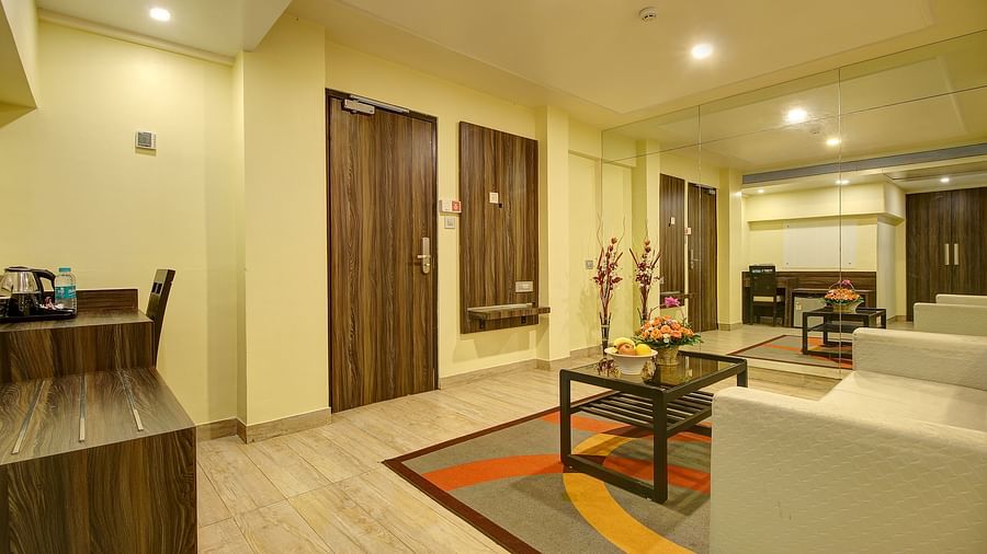 A bright hotel living area with glossy floors, a wooden shelf with a kettle, and water bottles.