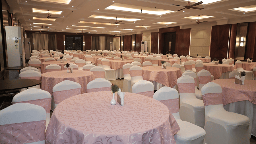 Luxury hotel ballroom featuring round table seating, soft decor, and modern lighting prepared for celebrations or meetings.