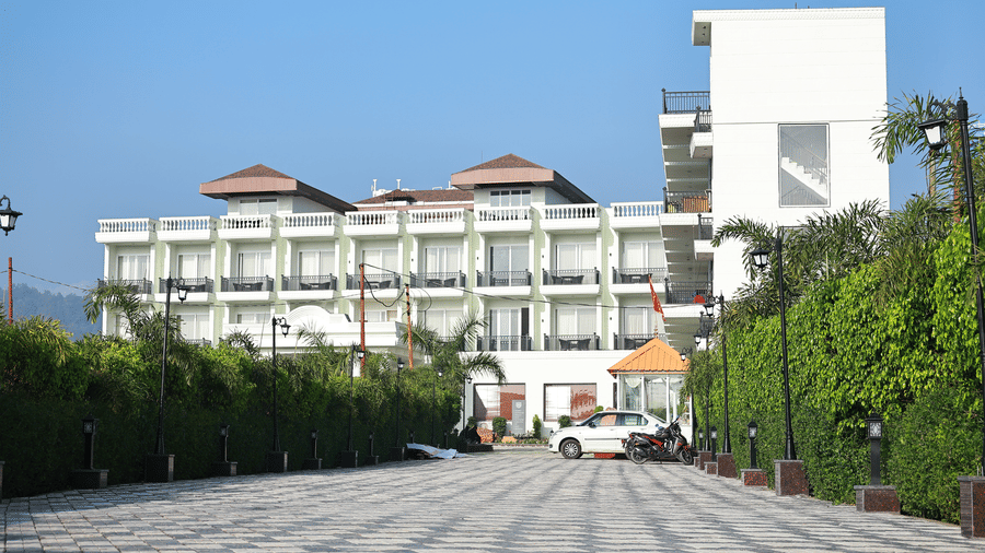 A clear view of the multi-story white hotel building with individual balconies, seen from the end of the paved driveway.