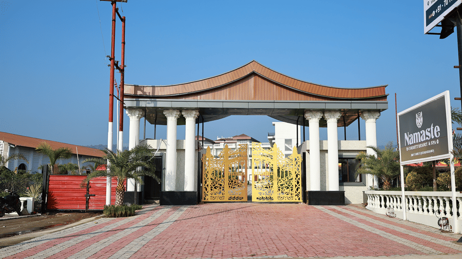 Grand entrance of Namaste Resort with gold filigree gates, white pillars, and a distinctive wooden pagoda-style roof.