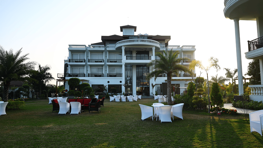 Front view of a white luxury hotel with balconies and white wicker seating on a manicured lawn.