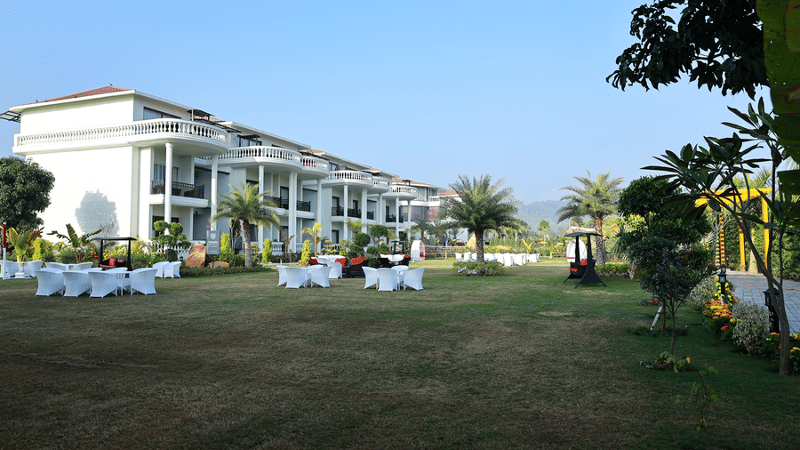Spacious green lawn with white outdoor seating sets and palm trees in front of white resort buildings.