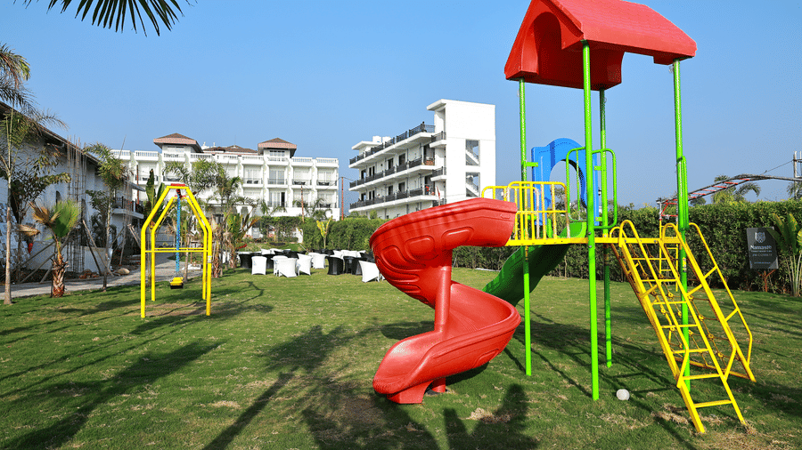 A bright children's playground with a red spiral slide and yellow climbing frame on a sunny resort lawn.
