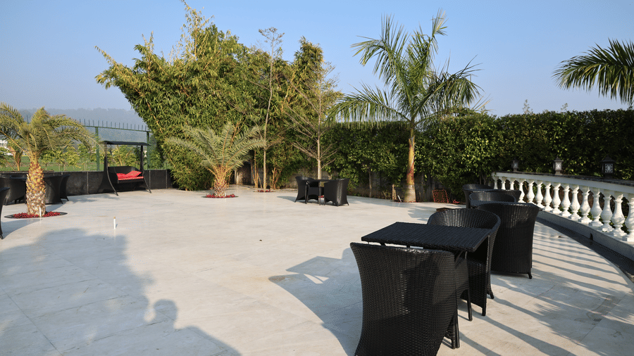 Spacious outdoor lounge area with modern wicker seating, tropical greenery, and a white balustrade.