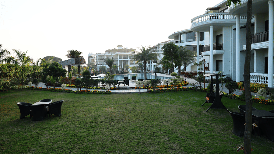Wide view of a resort courtyard with a swimming pool, curved white buildings, and black patio furniture.