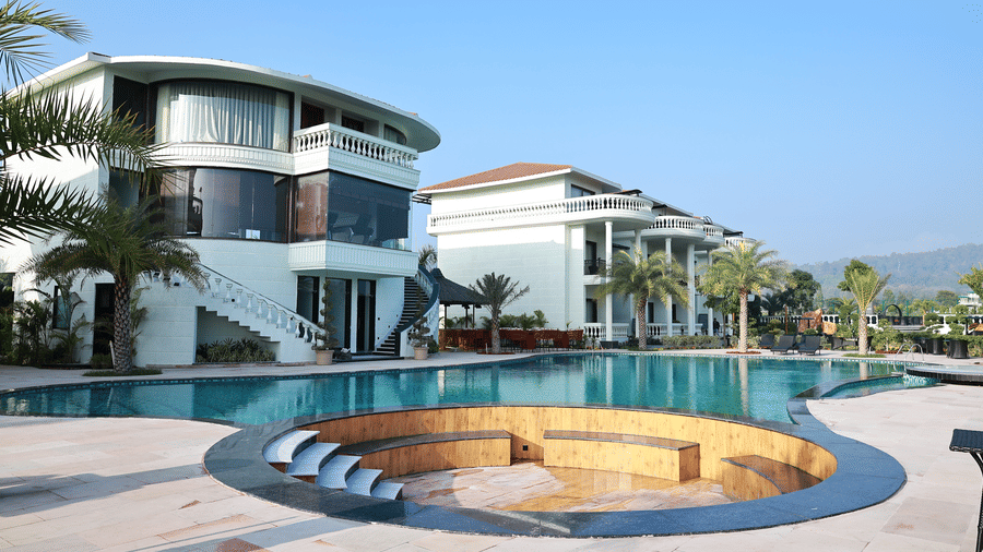 Modern resort with a large swimming pool, circular lounge area, and white villas under a clear blue sky.