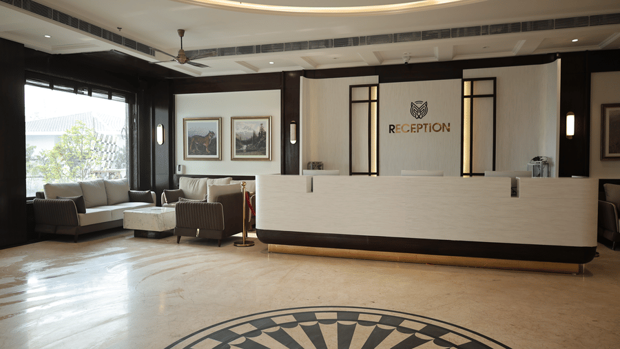 Elegant hotel reception desk with modern lighting, marble flooring, and comfortable lounge seating beside large windows.