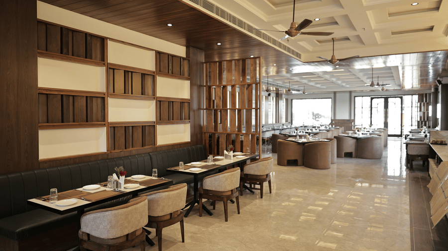 Elegant hotel restaurant interior with wooden accents, booth seating, and neatly arranged dining tables in a spacious setting.