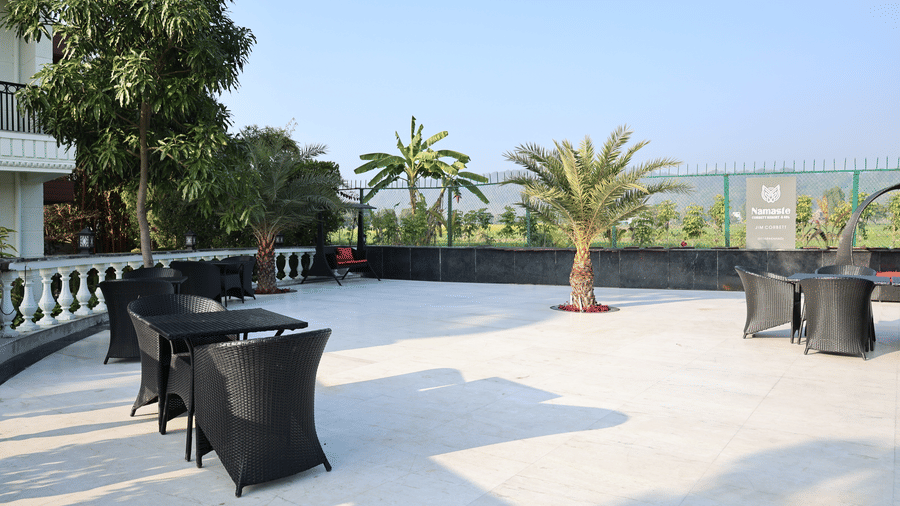 Open-air terrace with black wicker furniture, white marble flooring, and palm trees under a clear sky.