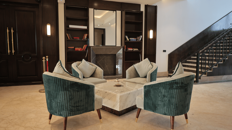 A lobby seating area with four upholstered chairs arranged around a marble table near a decorative fireplace.