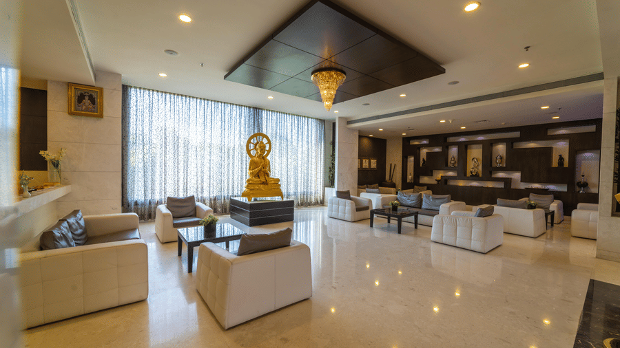Hotel lobby area with amble seating and warm lighting, and a statue of an idol in the centre at Narayani Heights Hotel & Resorts, Ahmedabad.