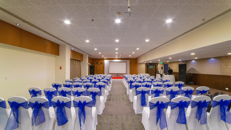Back view of a banquet setup with rows of white chairs adorned with blue sashes - Narayani Heights Hotel & Resorts