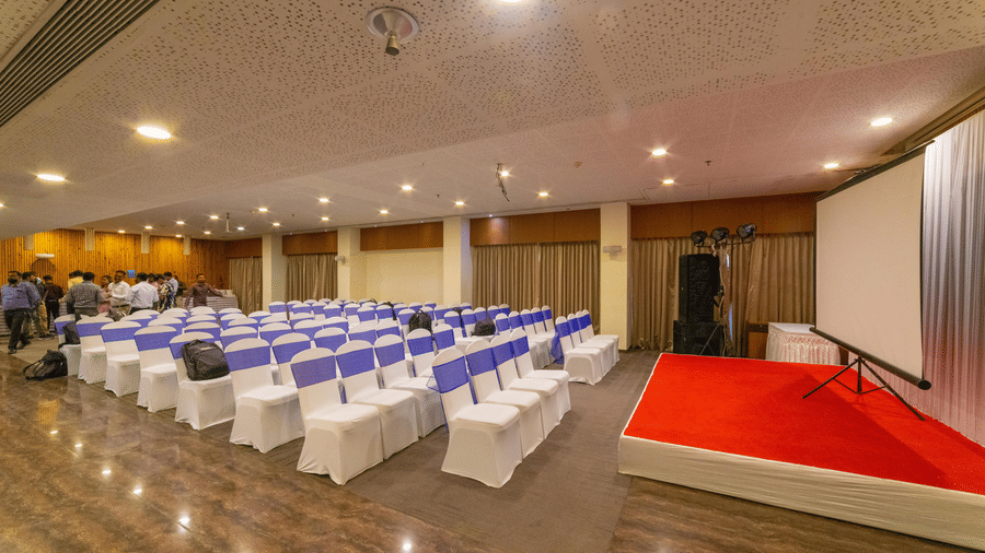 Well-lit banquet hall with theatre seating arrangement and red carpet stage setup - Narayani Heights Hotel & Resorts