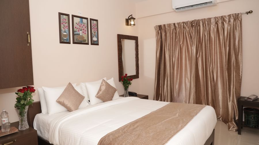 A bed with bedside tables, flowers, wall art, a mirror and window curtains at Nazri The Verda Hotel, Arambol.