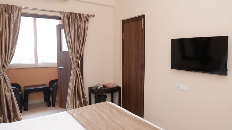 A bed near a window with curtains, a desk, chair and wall-mounted television at Nazri The Verda Hotel, Arambol.