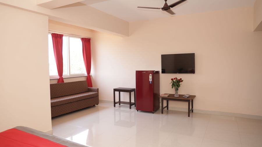 A corner view of a suite at Nazri The Verda Hotel, Arambol, showing a sofa, table with flowers, a TV, and a ceiling fan.