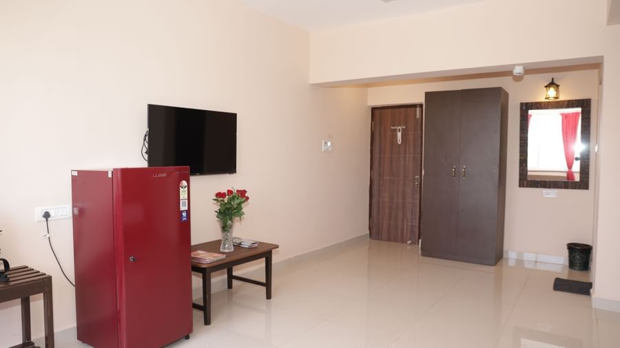 A spacious room at Nazri The Verda Hotel, Arambol, displaying a table with flowers, a TV mounted on the wall, and a red fridge.