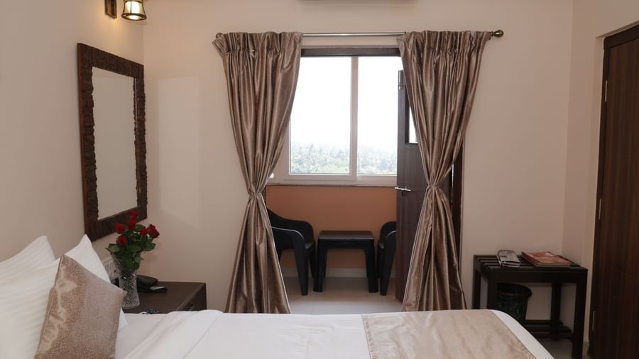 A bed facing a window with curtains, a desk, chair and mirror at Nazri The Verda Hotel, Arambol.