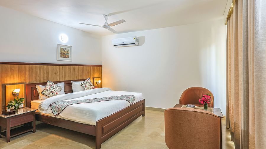 a double bed with side tables, lamps and chairs opposite it inside one of the rooms - Neer ganga Resorts