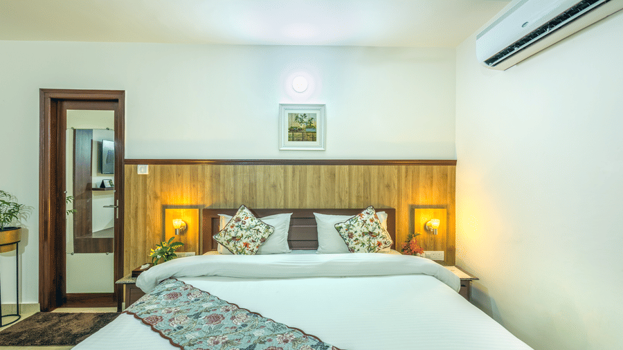 a double bed with a bed runner, side tables and lamps inside one of the rooms - Neer Ganga Resorts