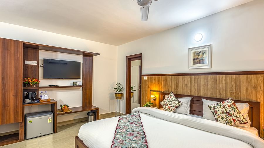 a double bed with side tables and lamps and a tv wall mounted next to it inside one of the rooms - Neer ganga Resorts
