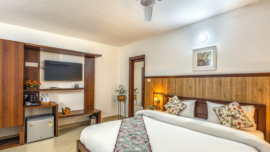 side view of a double bed with a tv wall mounted on the side inside one of the rooms - Neer Ganga Resorts