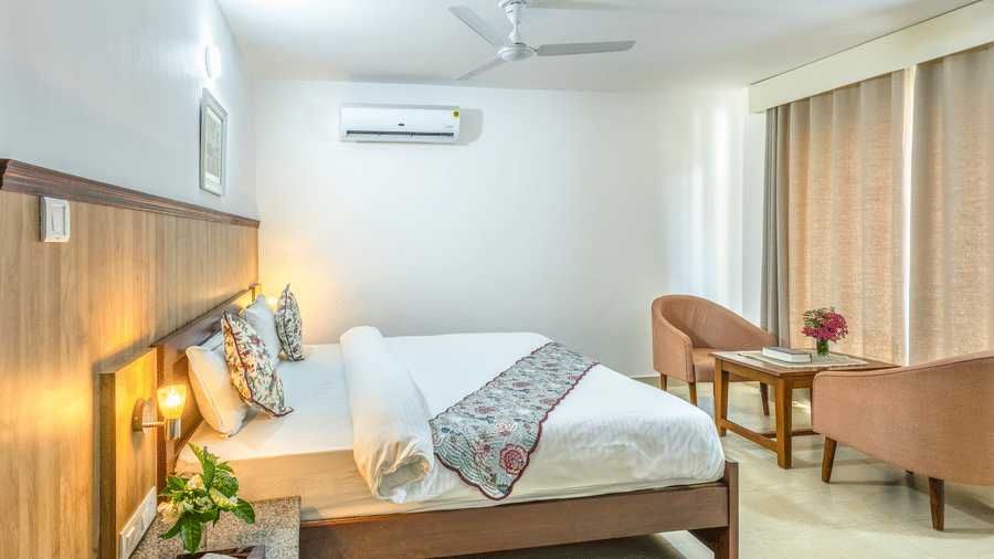 a double bed with side tables, lamps and chairs in front of it inside one of the rooms - Neer Ganga Resorts