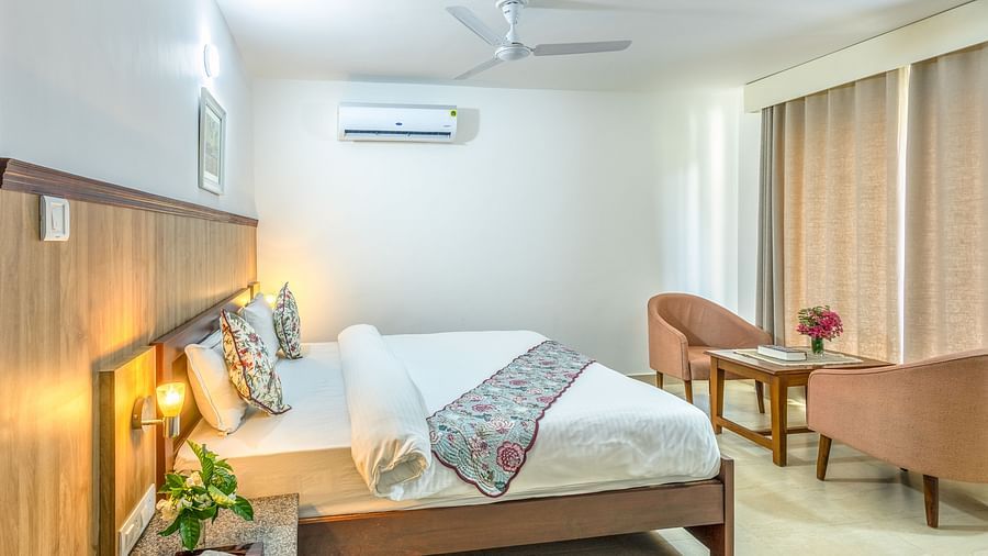 a double bed with side tables, lamps and chairs opposite it inside one of the rooms - Neer ganga Resorts