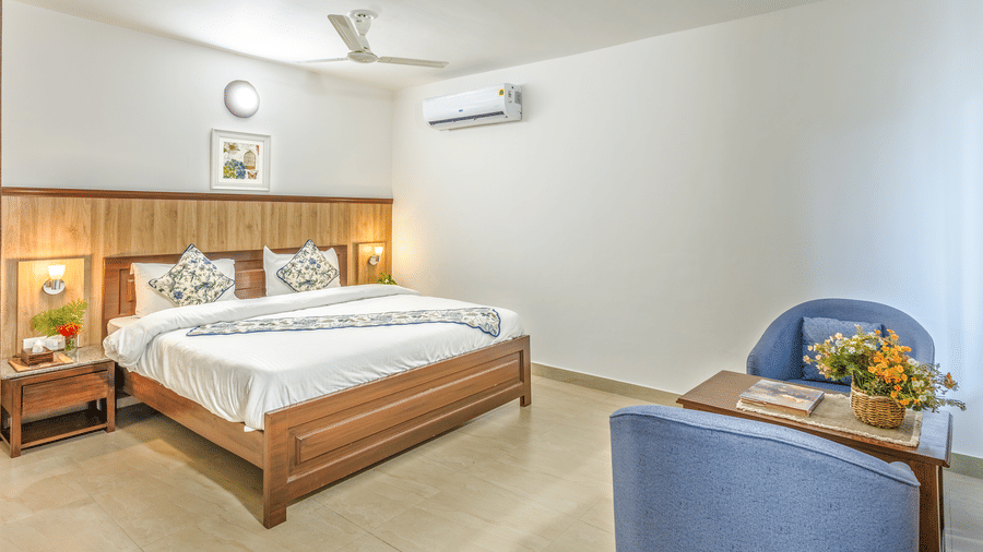a double bed with side tables, lamps and chairs in front of it inside one of the rooms - Neer Ganga Resorts