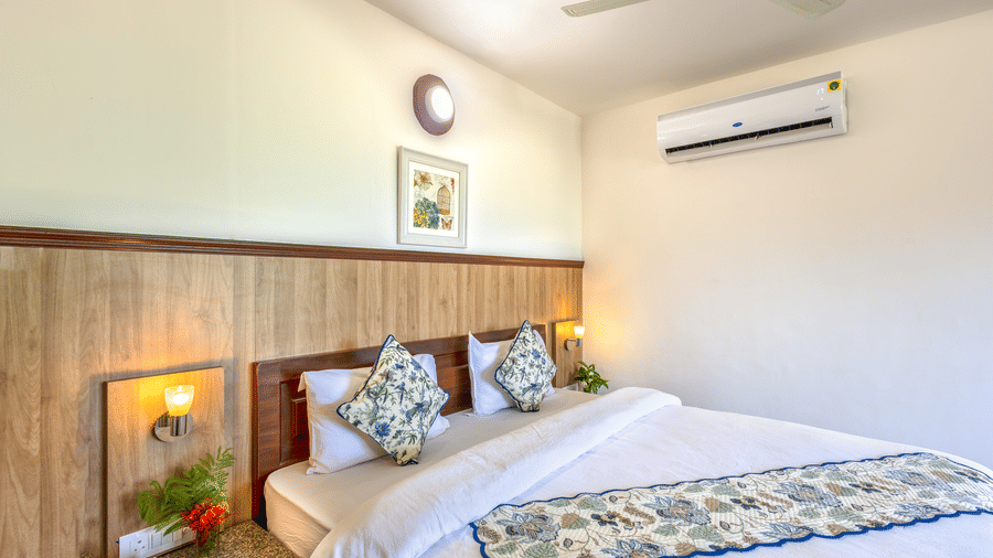 a double bed with side tables, lamps and an ac wall mounted inside one of the rooms - Neer Ganga Resorts