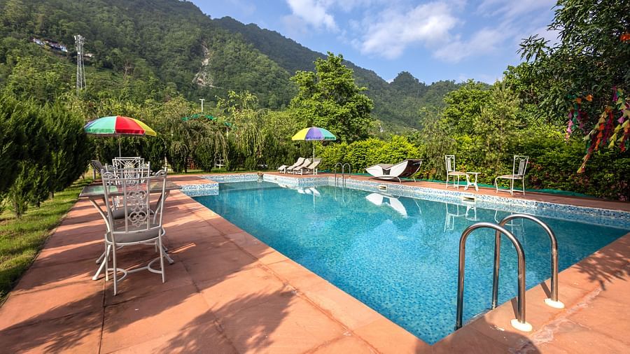 swimming pool with chairs, tables and canopies around it - neer ganga Resorts