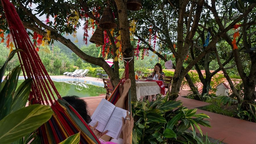 a woman sitting on a hammock reading a book while another women sitting on a table - neer ganga resorts