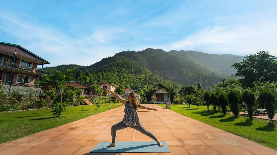 a woman doing yoga in an open area with a mountain in the background - Neer Ganga Resorts
