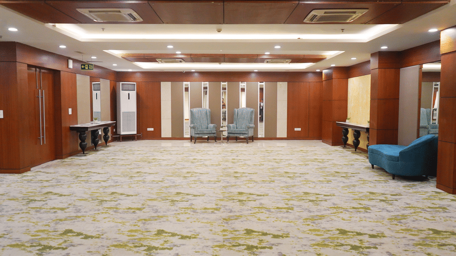 A spacious, empty meeting room with a patterned carpet, wooden pillars, and a single blue lounge chair in the corner.