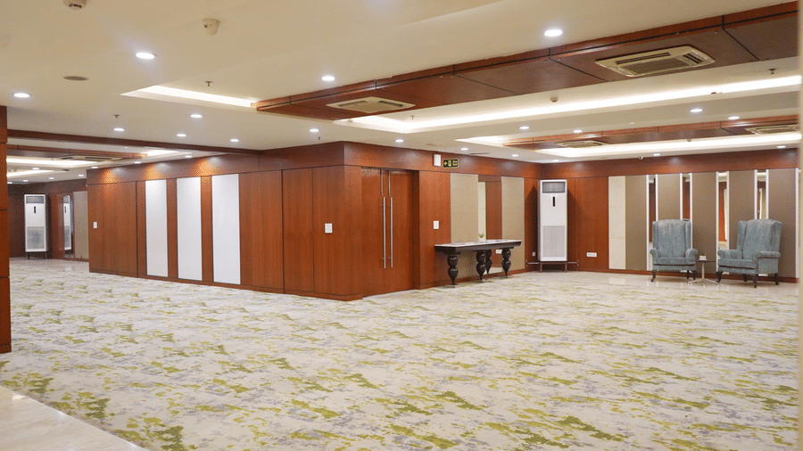 A wide-angle view of an expansive, empty hotel ballroom featuring wooden wall accents and a patterned green and beige carpet.
