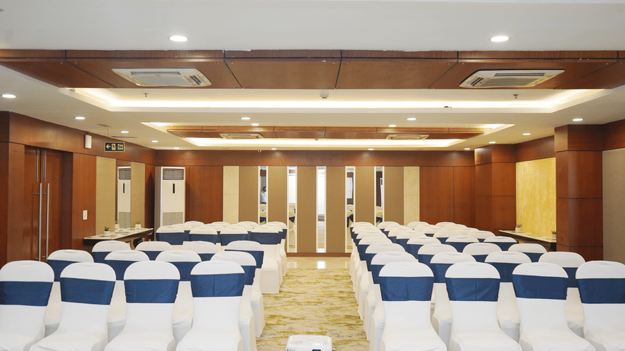 A wide view of an empty conference hall with neatly arranged theatre-style seating and rich wooden wall panels.