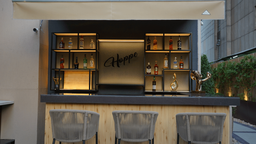 A modern outdoor bar counter setup with three grey barstools under a white fabric awning.