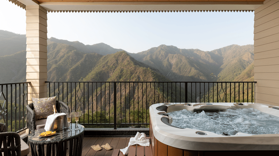 A private balcony featuring a bubbling outdoor hot tub and a seating area overlooking spectacular mountain ridges.