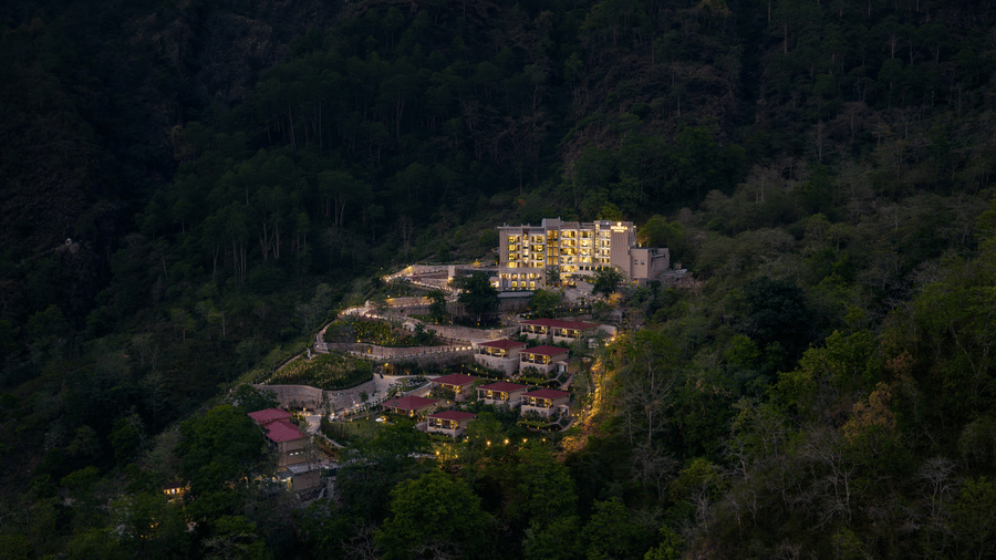 An aerial evening shot of a luxury resort brightly illuminated on a dark, dense forested hillside.