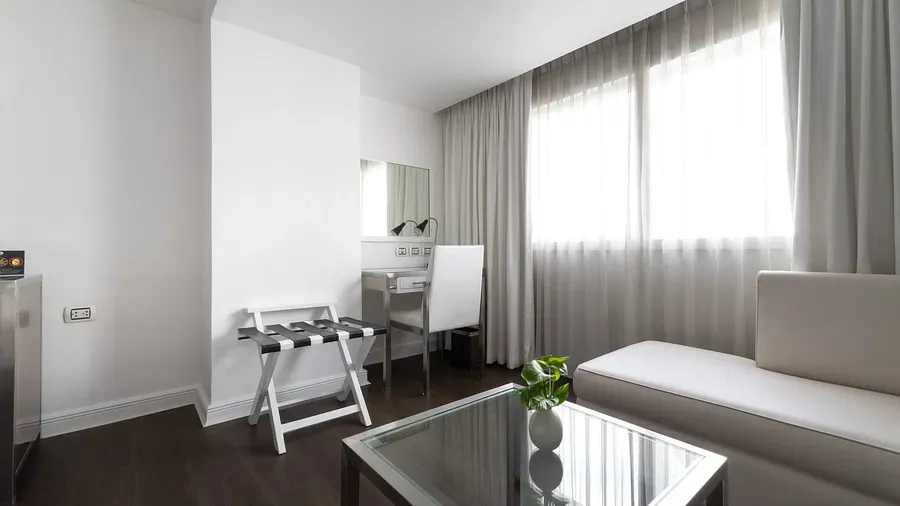 Minimalist hotel workspace with white desk, black checkered chair, cream sofa, glass table, and neutral decor creating a sophisticated ambience at Night Hotel Bangkok.